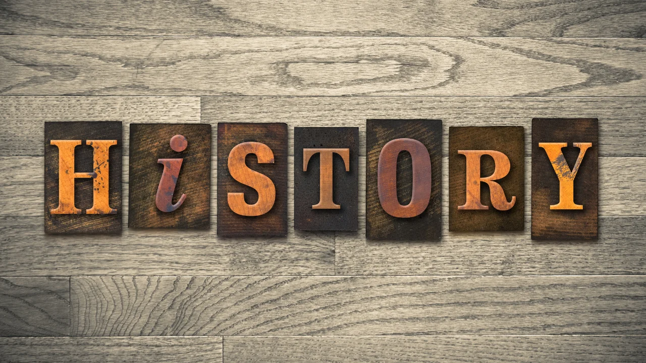 Rustic wooden letter blocks arranged on a wood‑grain surface to spell the word “HISTORY.”