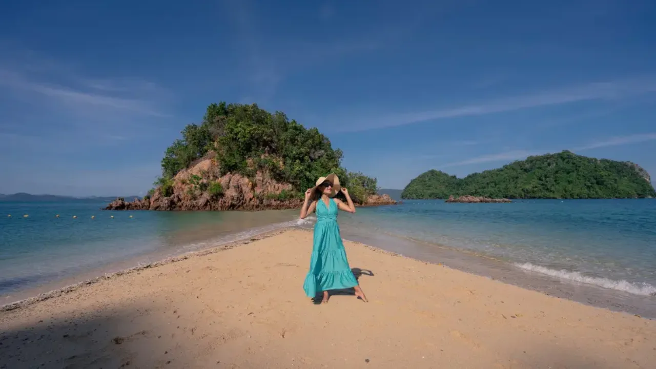 Woman in turquoise dress standing on a tropical sandbar between clear blue waters and lush green islands.

