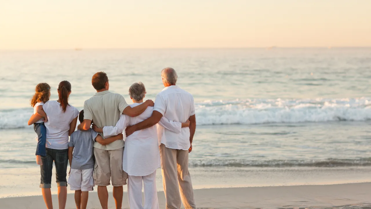A multigenerational family standing together on a serene beach in Andaman, watching the waves at sunset during a relaxing family vacation.