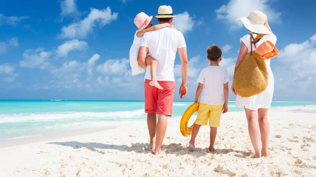 A family of four walking barefoot on a white sandy beach, gazing at the turquoise waters during a sunny day in Andaman.

