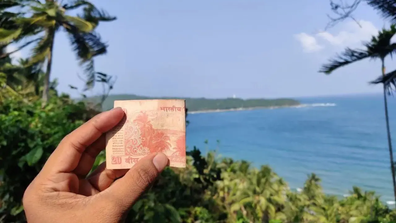 ₹20 note held against real-life backdrop of beach scenery